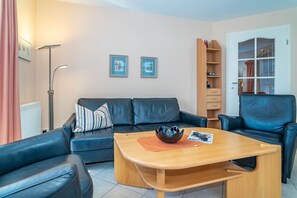 A living room with a black leather sofa, a wooden coffee table, and a bookshelf. - Ammerland Whg. 2 - Spacious 3-room apartment for up to 4 persons, with balcony. (Sylt)