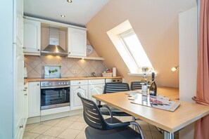 Une cuisine compacte avec des meubles blancs, un four encastré, une table à manger avec quatre chaises et une lucarne.