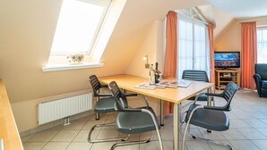 A dining area with a table, chairs, a television, and a window with curtains. - Ammerland Whg. 2 - Spacious 3-room apartment for up to 4 persons, with balcony. (Sylt)
