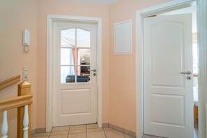 A hallway with two white doors, one with a window, and a wooden staircase.