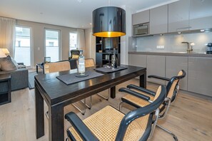 A modern dining area with a dark wooden table, four chairs with woven seats, and a large black pendant light.
