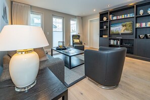 A modern living room with a sofa, a coffee table, a lamp, a bookshelf, and a television.