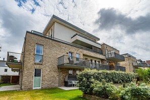 A modern two-story apartment with a brick facade, balconies, and a small garden area.