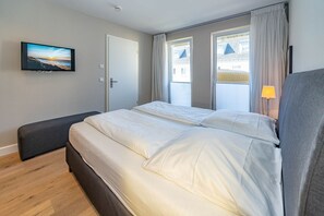 Una camera d'albergo moderna con un letto grande, una panca, una televisione e una finestra con tende.