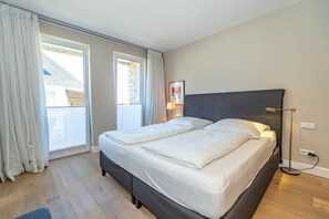 A modern bedroom with a large bed, two windows, and a view of a building. - Luxury Suite by the Sea, Apt. 17 - Luxury beachfront vacation apartment: relaxation and comfort (Sylt)