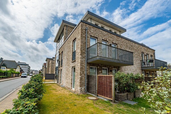 A modern two-story apartment with a balcony, brick exterior, and a small garden area.