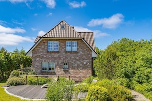 Une maison à deux étages, avec une façade en briques, de nombreuses fenêtres et un toit en pente.