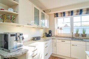 Eine moderne Küche mit weißen Schränken, einer Kaffeemaschine, einem Toaster und einem Fenster mit Blick auf ein Gewässer.