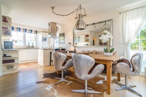 A modern kitchen with white cabinets, a central island, and a dining area with four chairs. - Maarwiet Hüs - Holiday home (detached house) for up to 6 persons with garden and (Wenningstedt-Braderup (Sylt))
