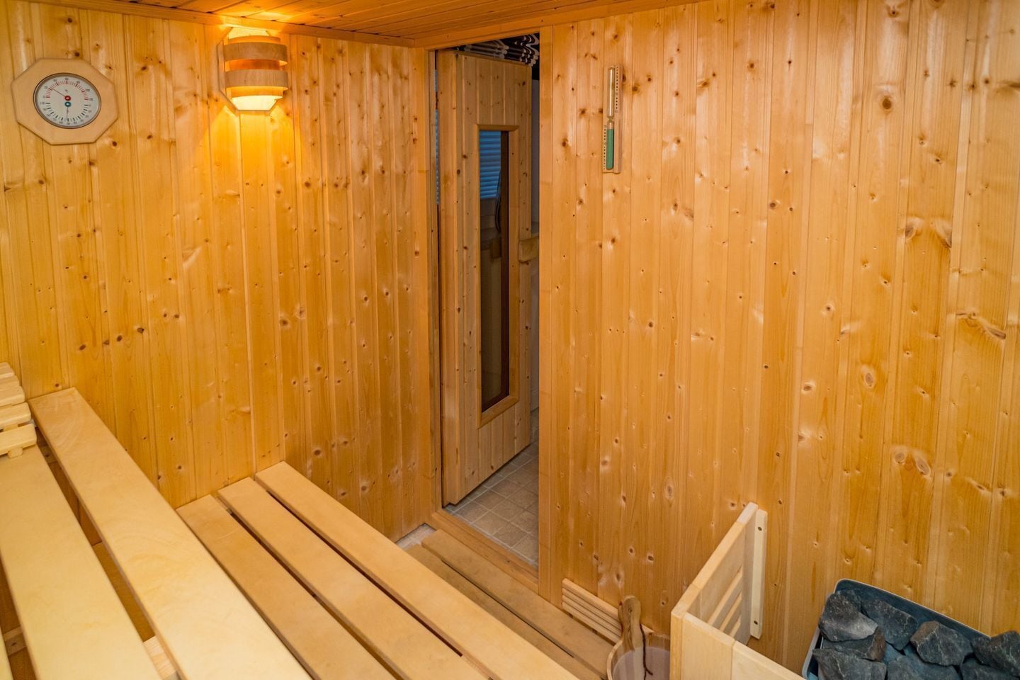 Un sauna en bois, doté de bancs et d’un thermomètre fixé au mur.