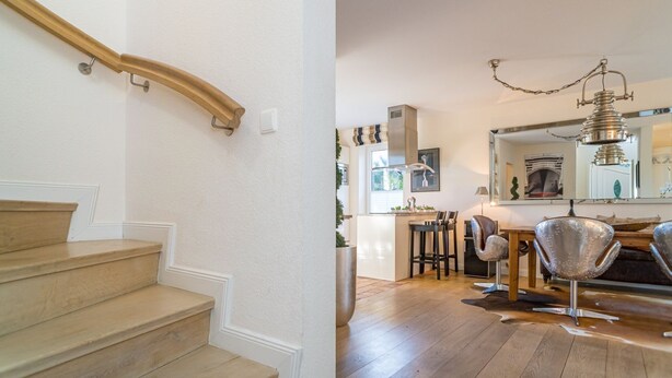 A staircase with wooden steps and a handrail, a kitchen with a dining area, and a chandelier.