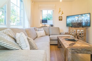 A living room with a sectional sofa, a wooden coffee table, a television, and a window with curtains. - Maarwiet Hüs - Holiday home (detached house) for up to 6 persons with garden and (Wenningstedt-Braderup (Sylt))