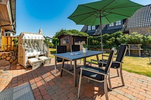 Un patio con mesa y sillas, una parrilla y un parasol verde.