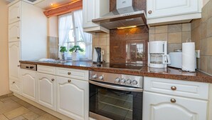 Une cuisine avec des meubles blancs, un four encastré, une machine à café et une fenêtre avec des rideaux.