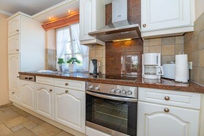 Eine Küche mit weißen Schränken, einem eingebauten Backofen, einer Kaffeemaschine und einem Fenster mit Vorhängen.