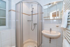 Un baño moderno con ducha envuelta en cristal, un lavabo blanco y un espejo sobre el lavabo.