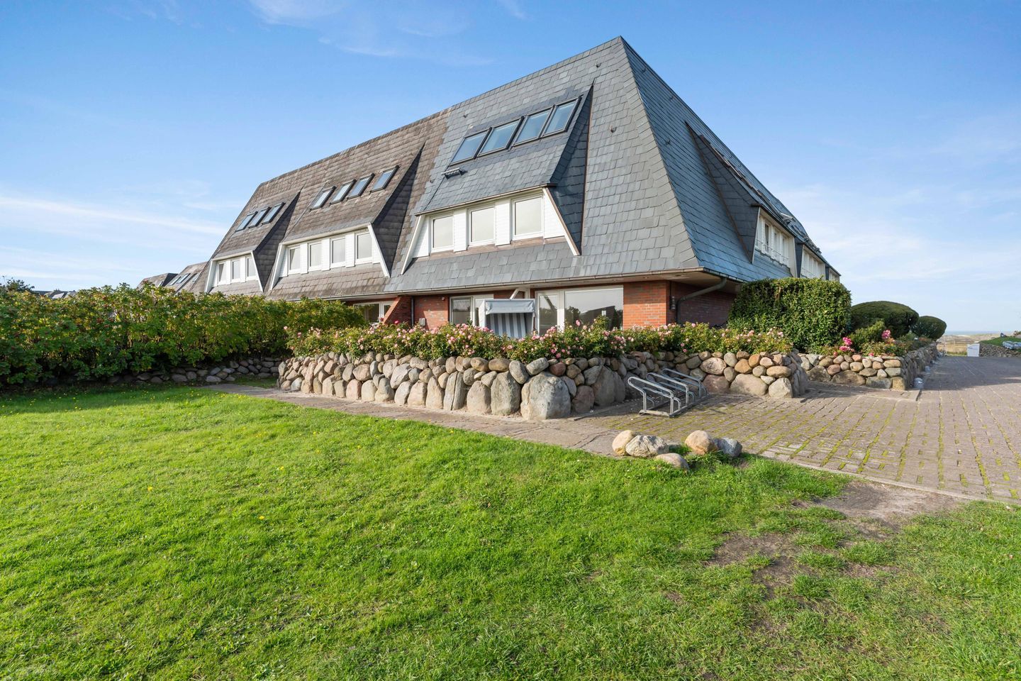 Een ruime, moderne woning met een schuin dak, een stenen muur en een verzorgd gazon.