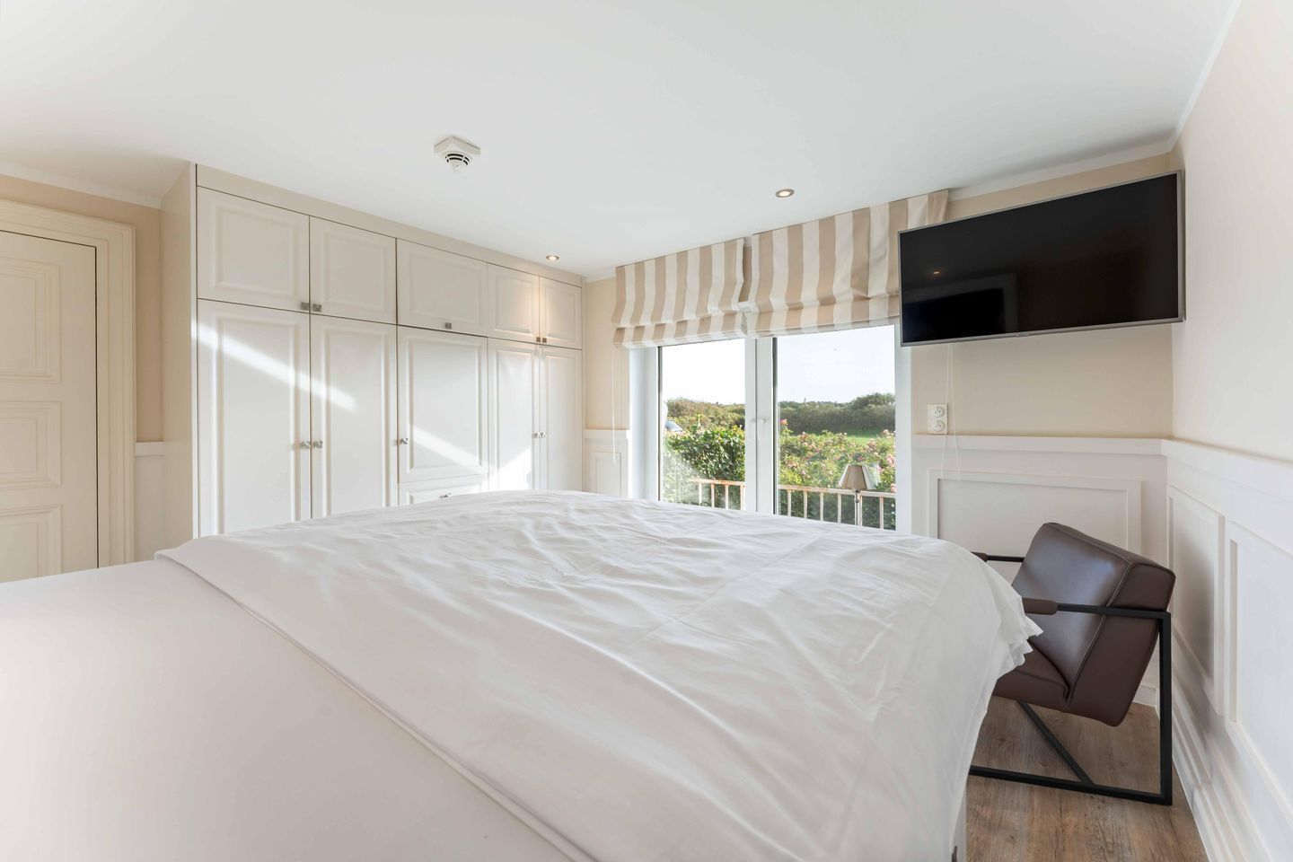 A bedroom with a large bed, wardrobe, and a TV mounted on the wall.