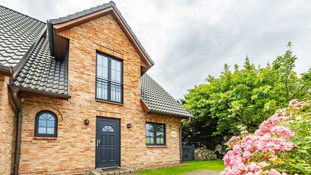 A two-story brick house with a black door, two windows, and a tiled roof. - Gode Stuv - Holiday home for up to 6 people with garden and sauna. (Sylt)
