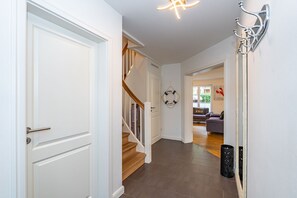 A hallway with a white door, a staircase, a wall-mounted light fixture, and a couch in the background.