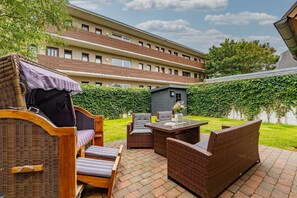 A patio area with wicker furniture, a table, and a small shed. - Gode Stuv - Holiday home for up to 6 people with garden and sauna. (Sylt)