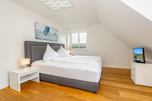 A bedroom with a bed, bedside table, lamp, TV, and a window with a view of the sea. - Gode Stuv - Holiday home for up to 6 people with garden and sauna. (Sylt)