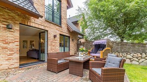 A patio with wicker furniture, a stone wall, and a view of a brick house. - Gode Stuv - Holiday home for up to 6 people with garden and sauna. (Sylt)
