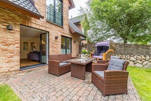 A patio with wicker furniture, a stone wall, and a view of a brick house.