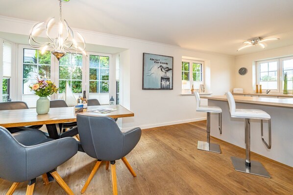 A modern kitchen with a wooden dining table, grey chairs, and a hanging light fixture.