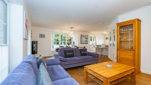 A living room with a sofa, a wooden coffee table, and a kitchen area with a cabinet and a dining table. - Gode Stuv - Holiday home for up to 6 people with garden and sauna. (Sylt)