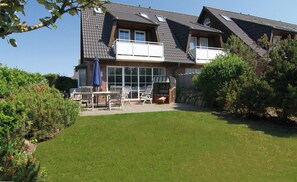 A two-story house with a balcony, a patio with outdoor furniture, and a well-maintained lawn.