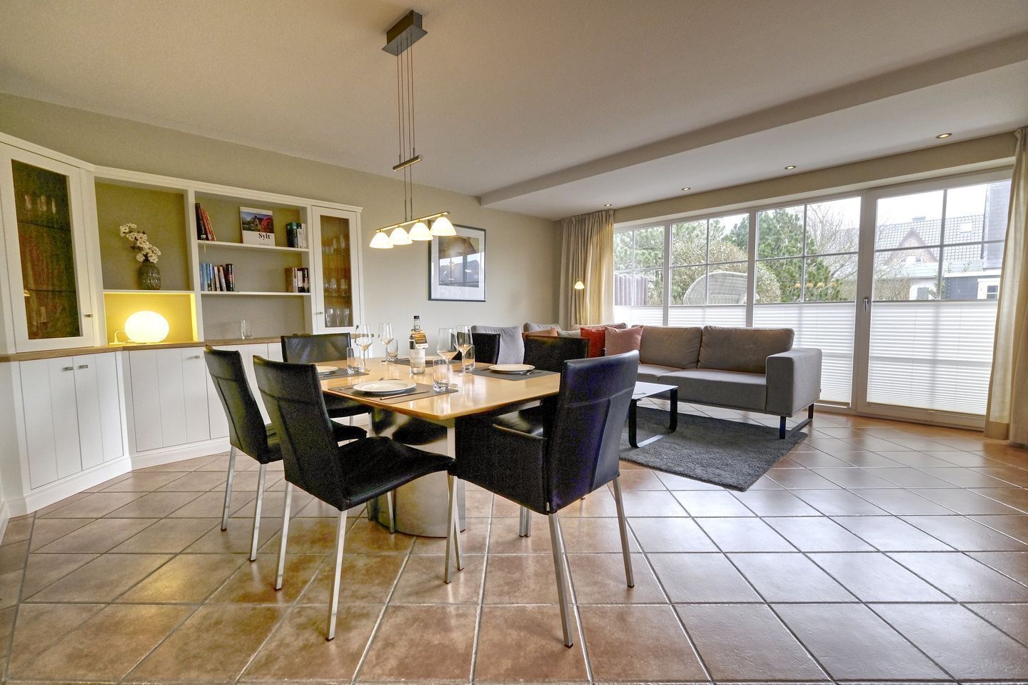 Een eethoek met een tafel voor vier personen, een bank en een groot raam met luxaflex.
