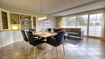 Een eethoek met een tafel voor vier personen, een bank en een groot raam met luxaflex.