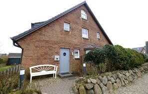 Une maison en briques avec une porte grise, un banc blanc et un mur en pierre.