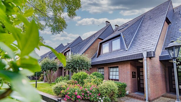 Una hilera de casas con techos inclinados y fachadas de ladrillo, rodeadas de jardines cuidados y un cielo despejado.