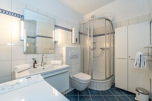 Un baño moderno con un lavamanos blanco, un inodoro, una cabina de ducha y un espejo.