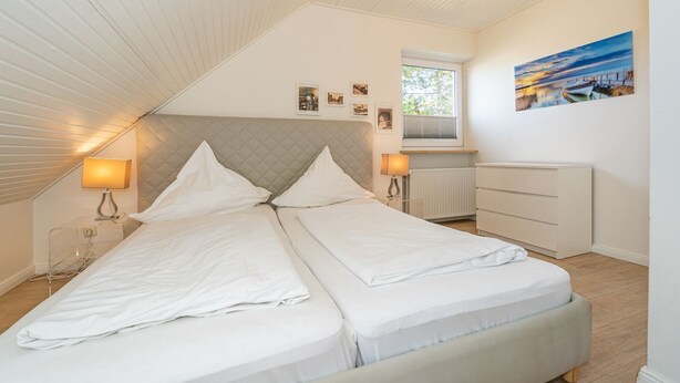 A bedroom with a bed, bedside lamps, a dresser, a window, and a painting on the wall. - App.syltperle - Helle Wohnung Ruhig Gelegen in Westerland (Sylt)