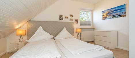 A bedroom with a bed, bedside lamps, a dresser, a window, and a painting on the wall.