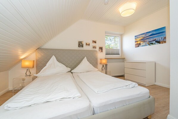 A bedroom with a bed, bedside lamps, a dresser, a window, and a painting on the wall. - App.syltperle - Helle Wohnung Ruhig Gelegen in Westerland (Sylt)
