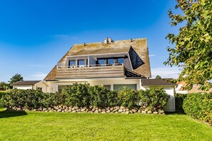 A modern house with a sloped roof, large windows, and a stone foundation. - App.syltperle - Helle Wohnung Ruhig Gelegen in Westerland (Sylt)