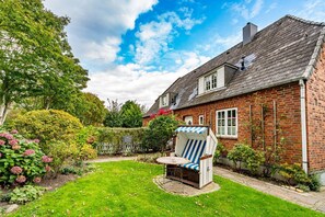 A brick house with a garden, a blue and white striped chair, and a clear sky.