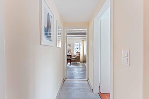 Een gang met kunstwerken in lijsten aan de muren, die leidt naar een kamer met een bureau en stoel.