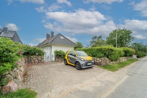 A compact car parked in front of a house with a stone wall and a paved driveway. - Söns-rose - Luxusoase mit Traumhaften Garten in Munkmarsch am Wattenmeer (Sylt-Ost)