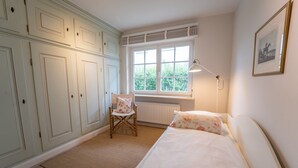 Ein Schlafzimmer mit Bett, Stuhl, Heizkörper, Fenster und einem Bild an der Wand.