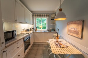 Ett kompakt kök med vita skåp, en mikrovågsugn, ett handfat och en matplats med ett bord och en bänk.