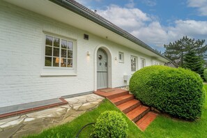Ein weißes Haus aus Backstein mit einem Kiesweg, der zur Haustür führt, einem gepflegten Rasen und einem großen, grünen Busch.