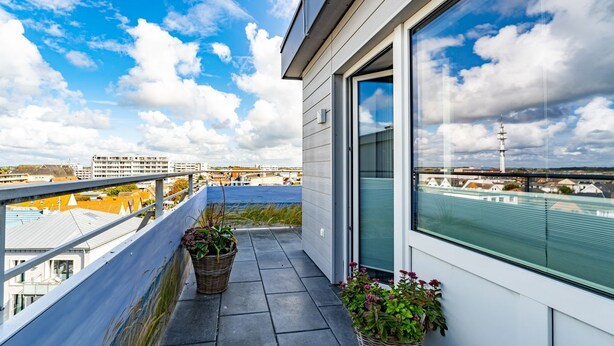A balcony with two wicker baskets containing plants, a clear view of the cityscape, and a large window with a view of a tower.