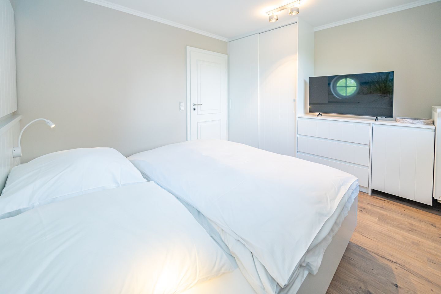 Een slaapkamer met een bed, een bedlampje, een kledingkast en een televisie op een dressoir.