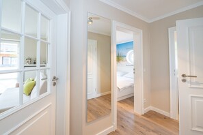 A hallway with white doors, a mirrored wall, and a bed with a view of the sky.