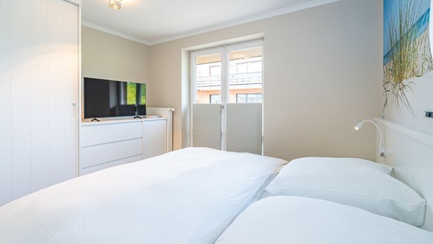 Un dormitorio con cama, televisor, radiador y ventana con persianas.